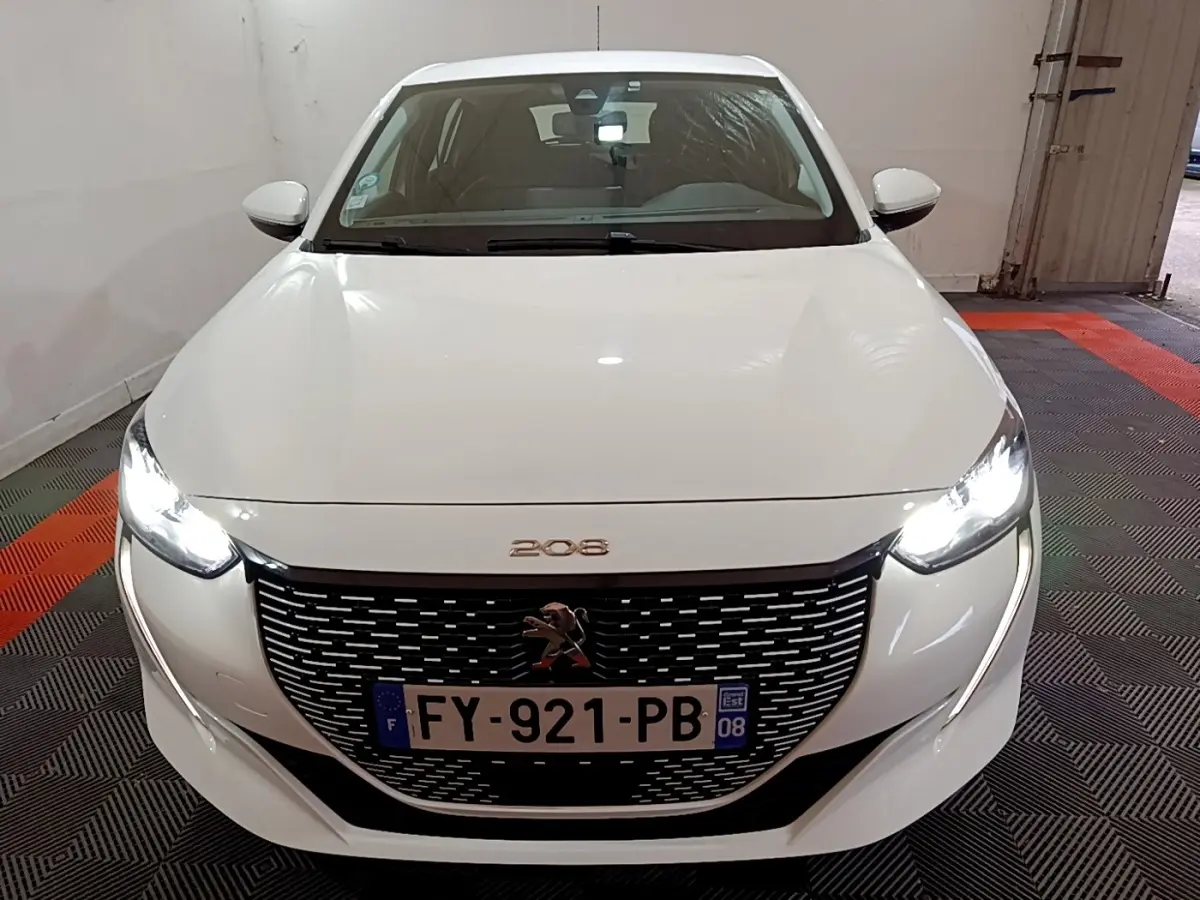 Vue frontale d'une Peugeot 208 électrique blanche avec phares LED allumés et calandre noire distinctive.
