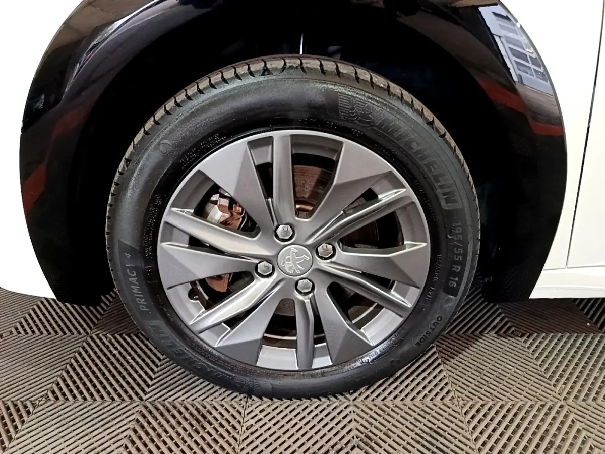 Gros plan sur la roue avant droite d'une Peugeot 208 électrique blanche, avec jante alliage gris et pneu Michelin.