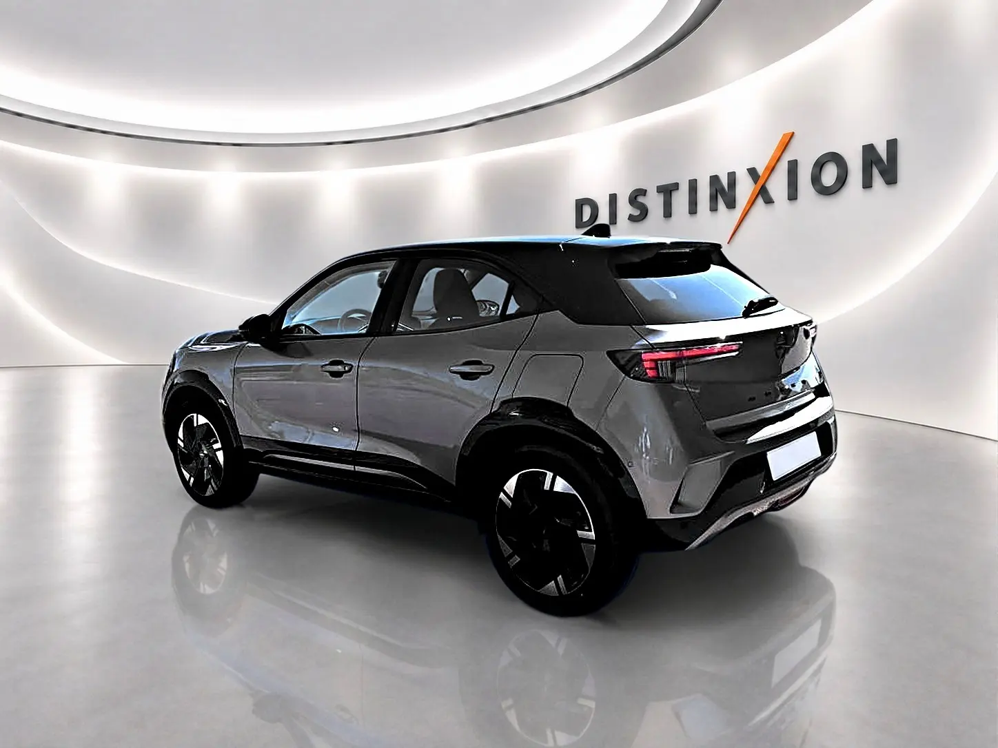 Opel Mokka Electric gris en 3/4 arrière droit, avec jantes alu noires et toit noir contrasté dans un showroom lumineux.
