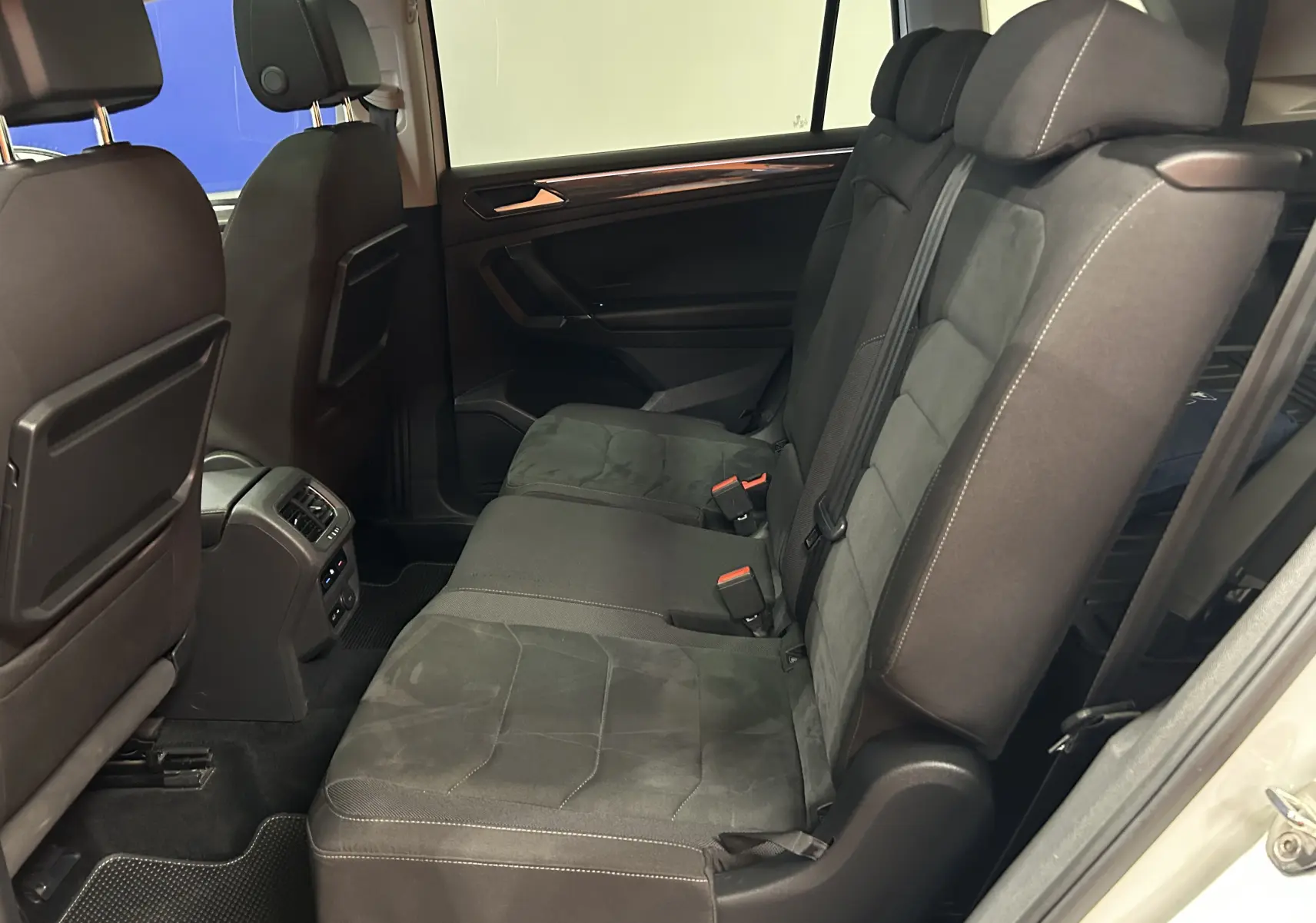 Vue latérale intérieure des sièges arrière noirs en tissu du Volkswagen Tiguan Allspace blanc, avec accoudoirs et ceintures visibles.