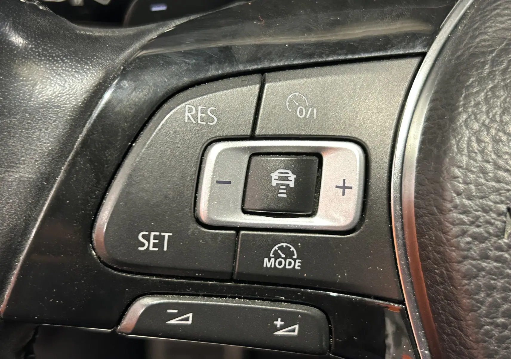 Gros plan sur les commandes de régulateur de vitesse au volant noir du Volkswagen Tiguan Allspace blanc 2018.