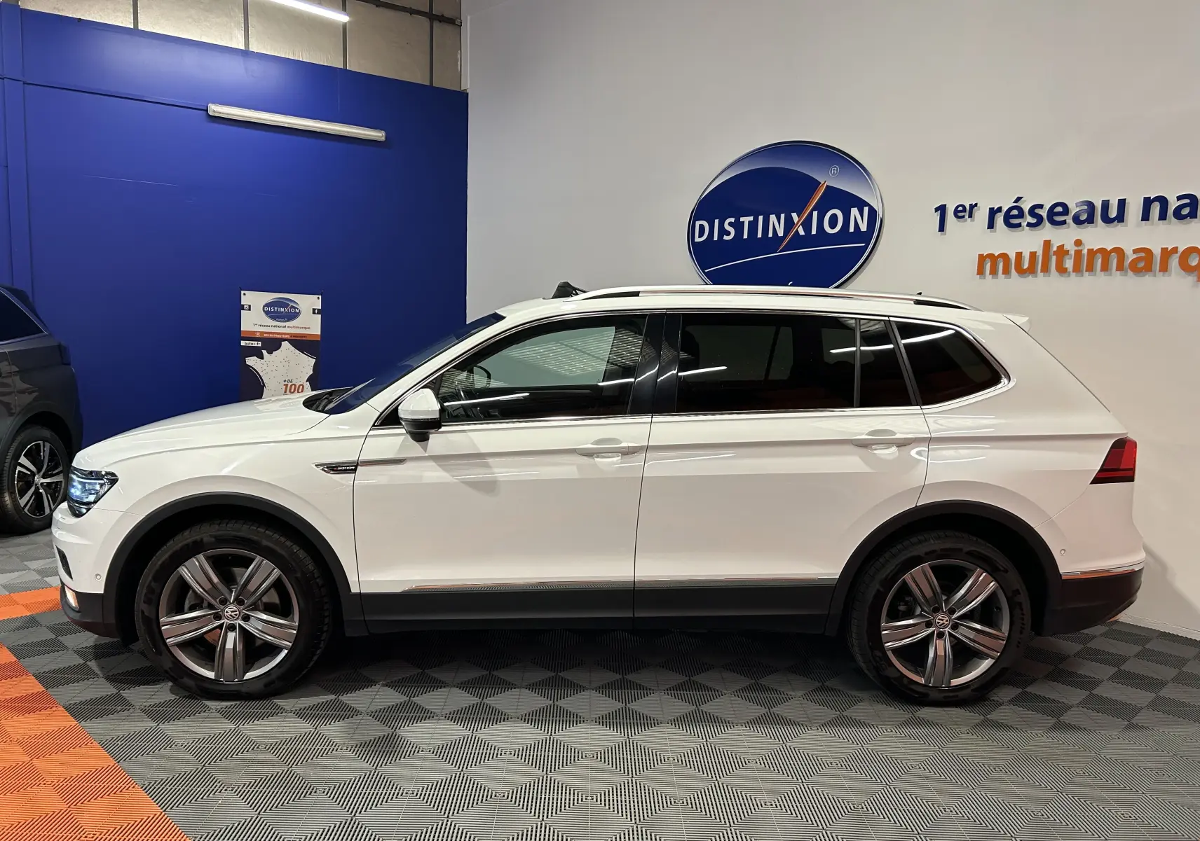 Profil latéral droit d'un Volkswagen Tiguan Allspace blanc 2018 avec jantes alliage et vitres teintées en showroom.