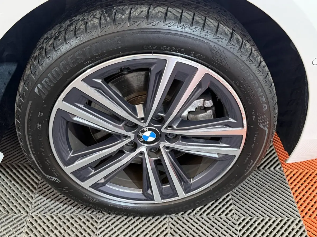 Gros plan sur la roue avant droite d'une BMW Série 1 blanche avec jante alliage bicolore et logo BMW central.