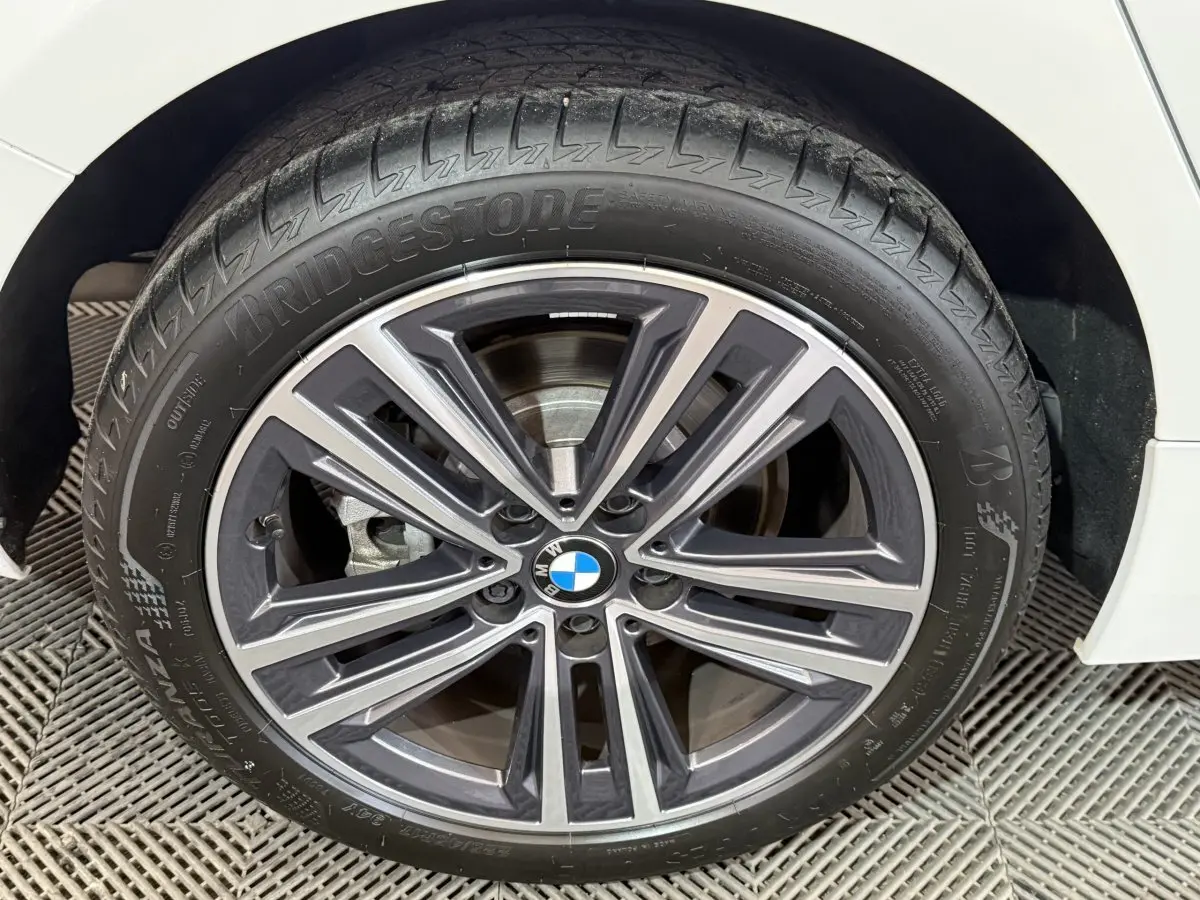 Gros plan sur la roue avant droite d'une BMW Série 1 blanche, avec jante alliage et logo BMW central visible.