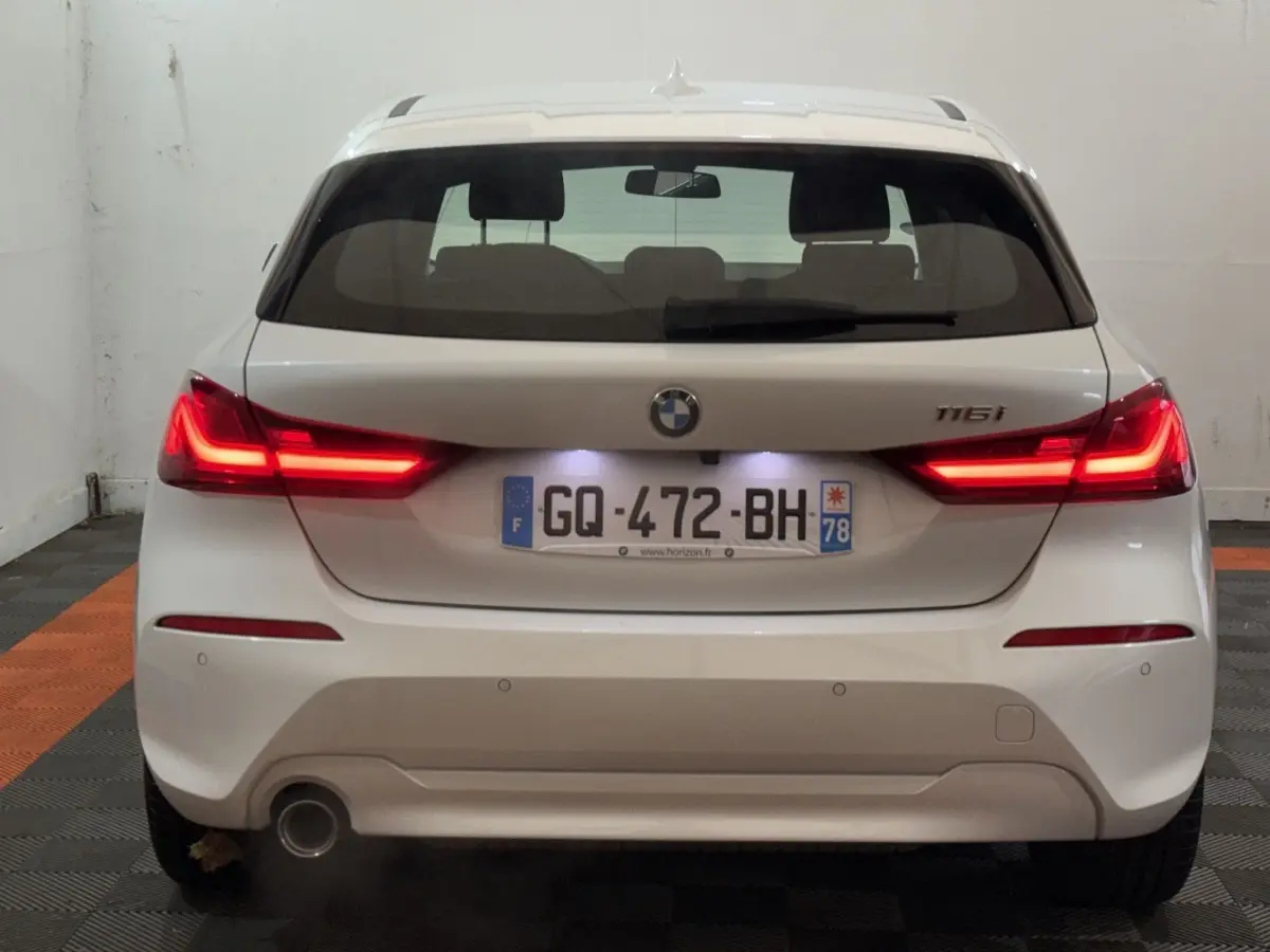 Vue arrière d'une BMW Série 1 116i blanche avec feux LED allumés et plaque d'immatriculation française.