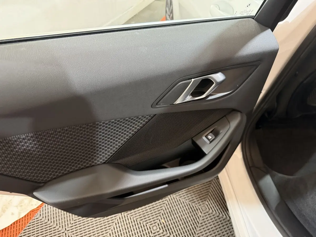 Gros plan sur la porte avant gauche noire avec poignée argentée et bouton de lève-vitre d'une BMW Série 1 blanche 2023.