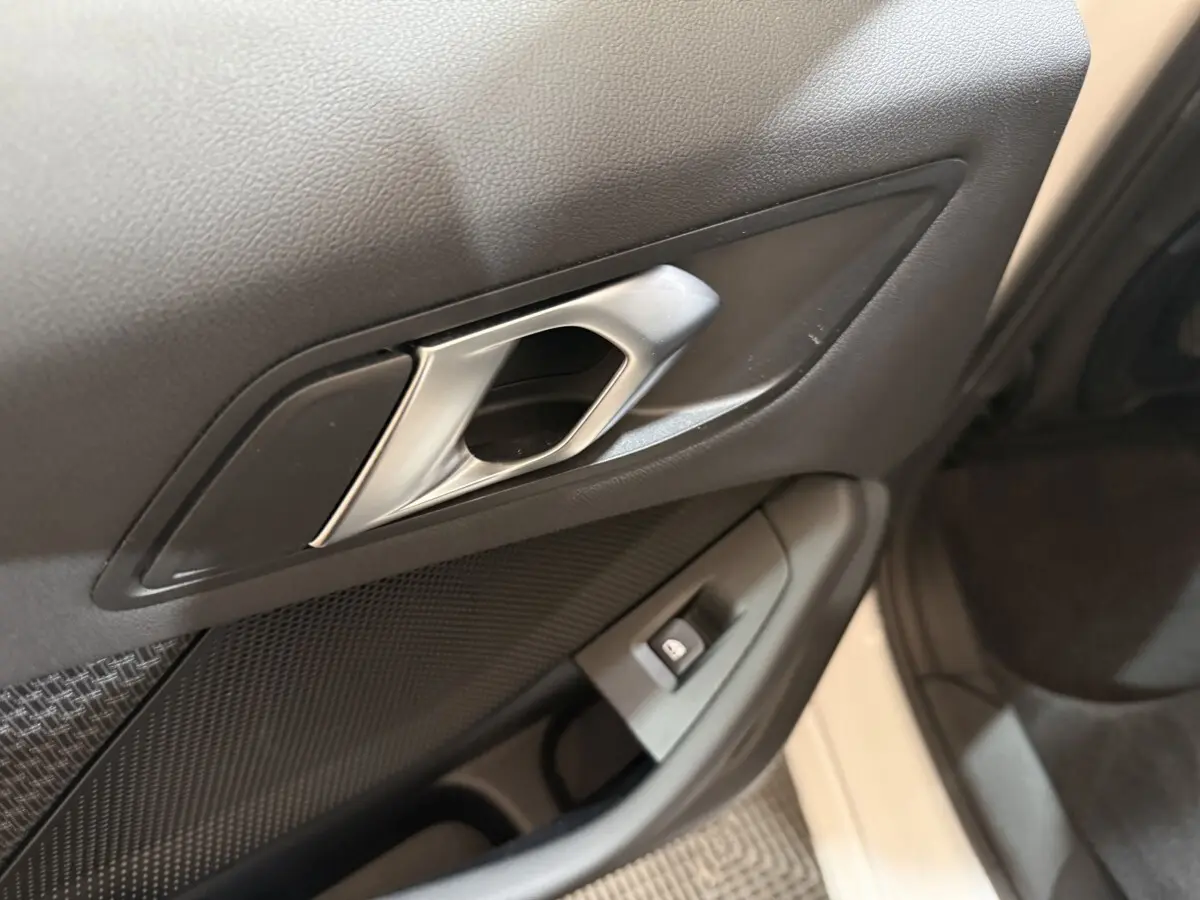 Gros plan sur la poignée intérieure côté droit de la porte d'une BMW Série 1 blanche, avec bouton de verrouillage.