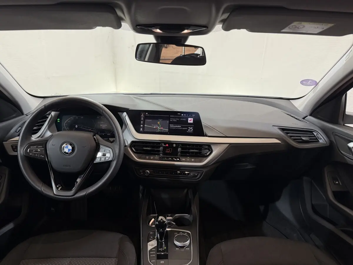 Tableau de bord et volant cuir BMW Série 1 116i 2023 vus de face, avec écran tactile central et commandes modernes.