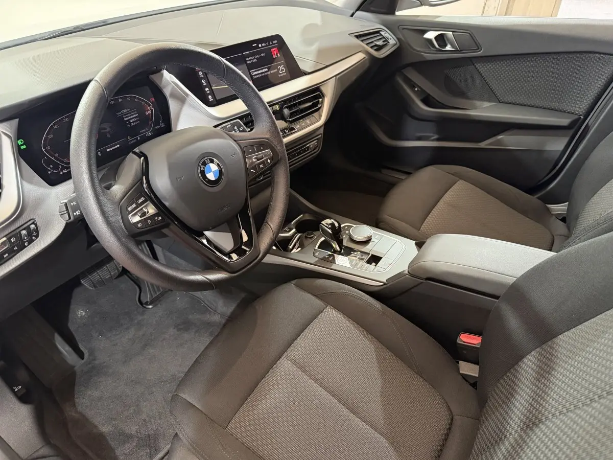 Intérieur de la BMW Série 1 116i 2023 vu côté conducteur, volant cuir et écran tactile 10,25 pouces visibles.