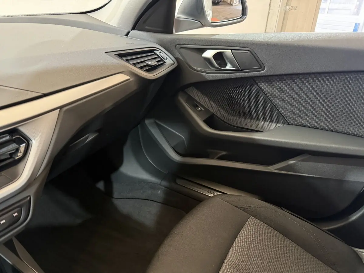 Intérieur côté passager de la BMW Série 1 116i blanc, montrant la porte et le tableau de bord noir avec détails tissu.