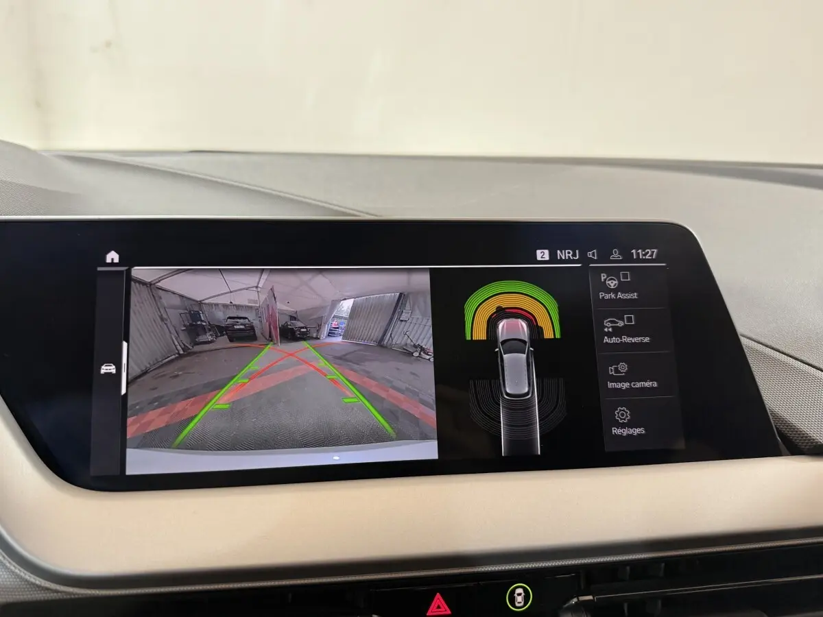 Écran tactile central de la BMW Série 1 blanche 116i DKG7 montrant l'aide au stationnement arrière en intérieur.