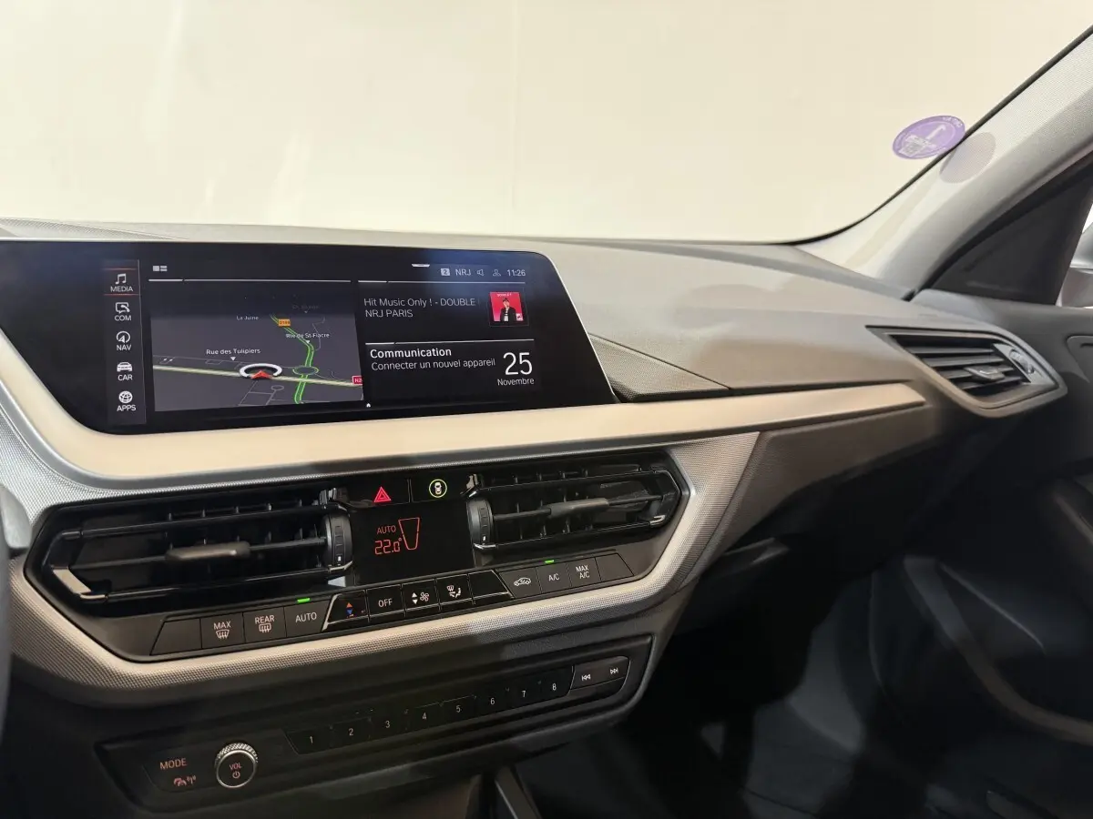 Tableau de bord de BMW Série 1 116i blanc, vue intérieure côté passager avec écran tactile et commandes climatisation.