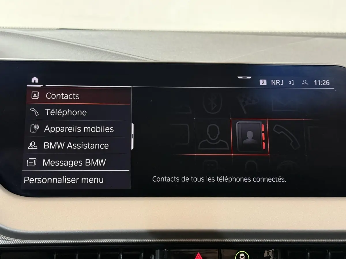 Écran tactile central de la BMW Série 1 blanche 116i DKG7 Business Design affichant le menu contacts.