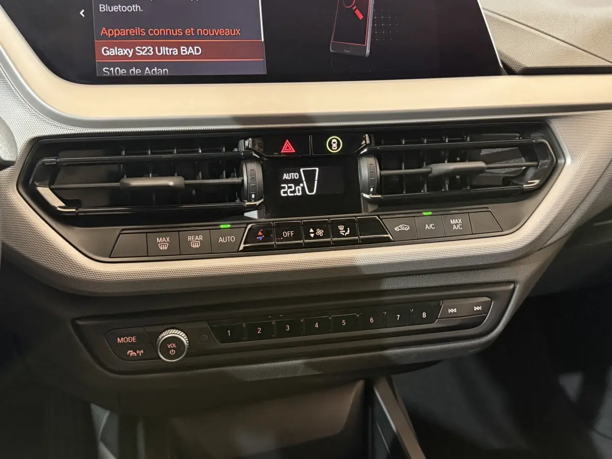 Vue rapprochée du tableau de bord noir de la BMW Série 1 116i 2023 avec commandes climatisation et écran tactile.