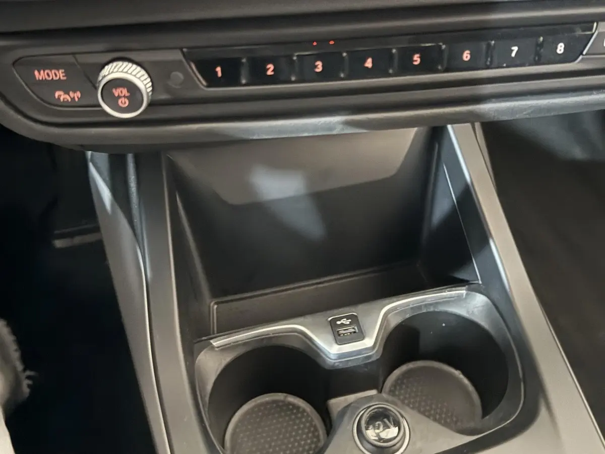Gros plan sur la console centrale noire de la BMW Série 1 116i avec porte-gobelets et commandes audio visibles.