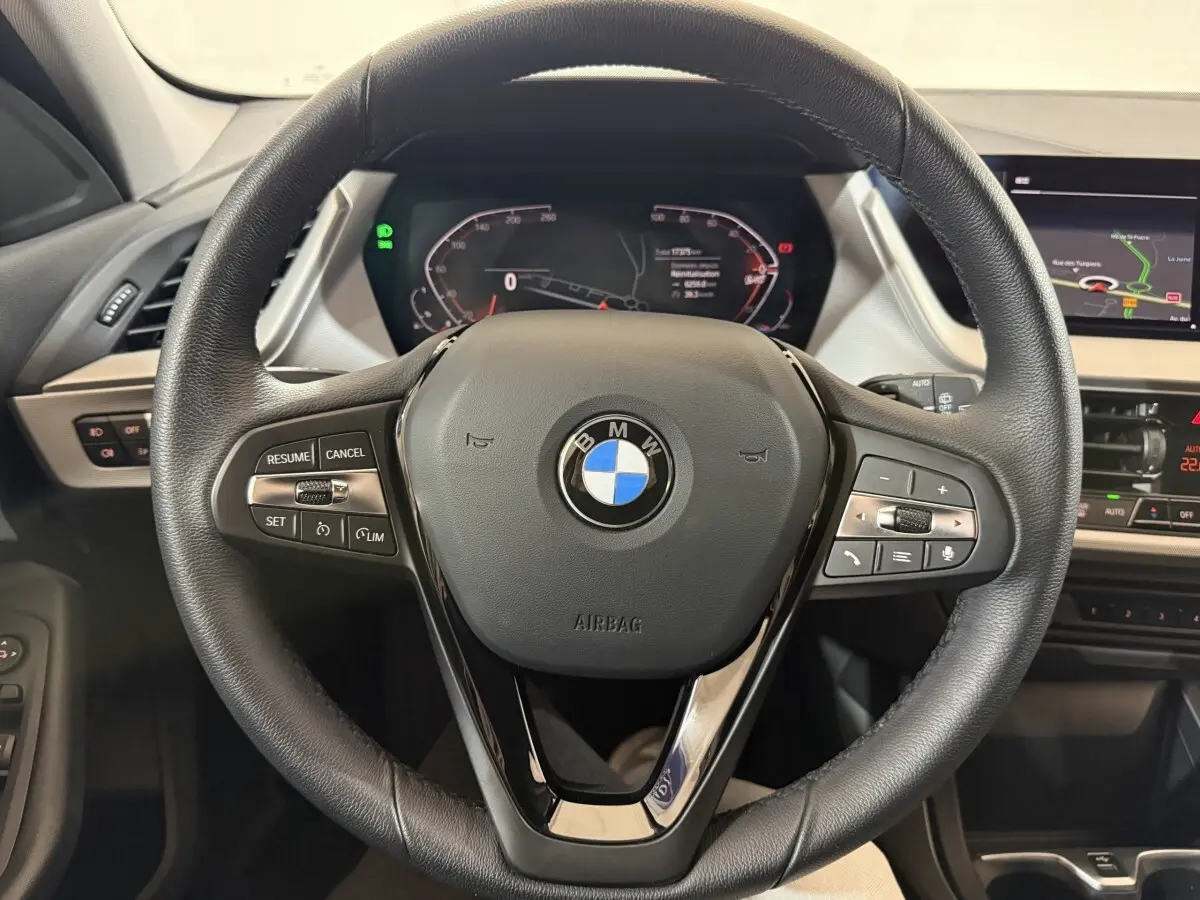 Vue rapprochée du volant cuir noir de la BMW Série 1 116i 2023 avec tableau de bord digital et écran tactile.