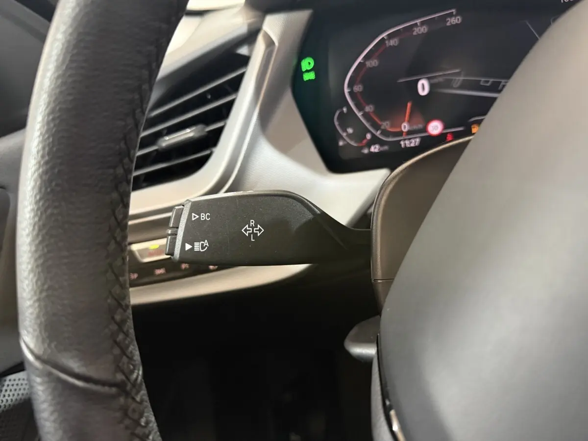 Gros plan sur la manette de clignotants noire à gauche du volant cuir dans le tableau de bord numérique d'une BMW Série 1 blanche 2023.