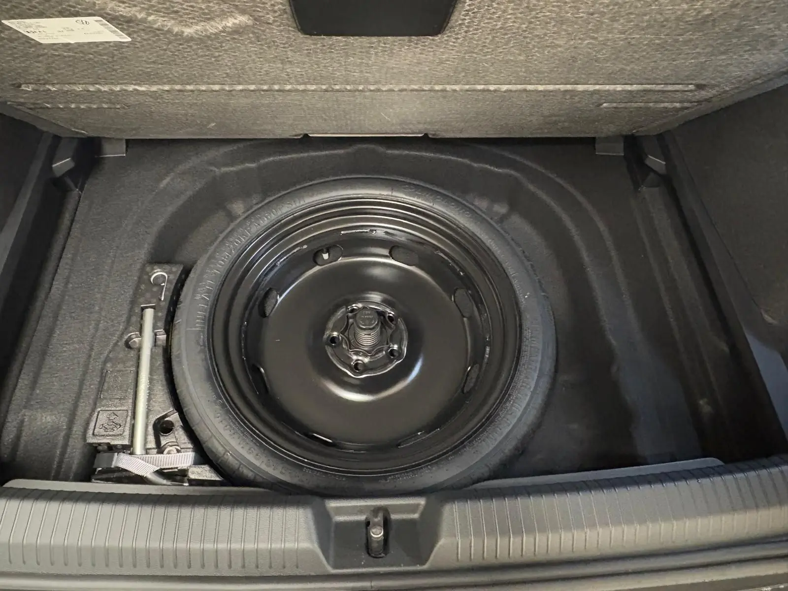 Vue plongeante sur la roue de secours compacte noire et le cric dans le coffre d'une Volkswagen Golf 2.0 TDI 150 DSG7.