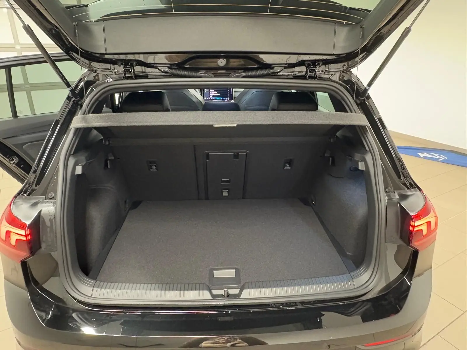 Vue arrière du coffre ouvert d'une Volkswagen Golf 2.0 TDI noire, montrant l'espace de chargement vide et les feux arrière allumés.