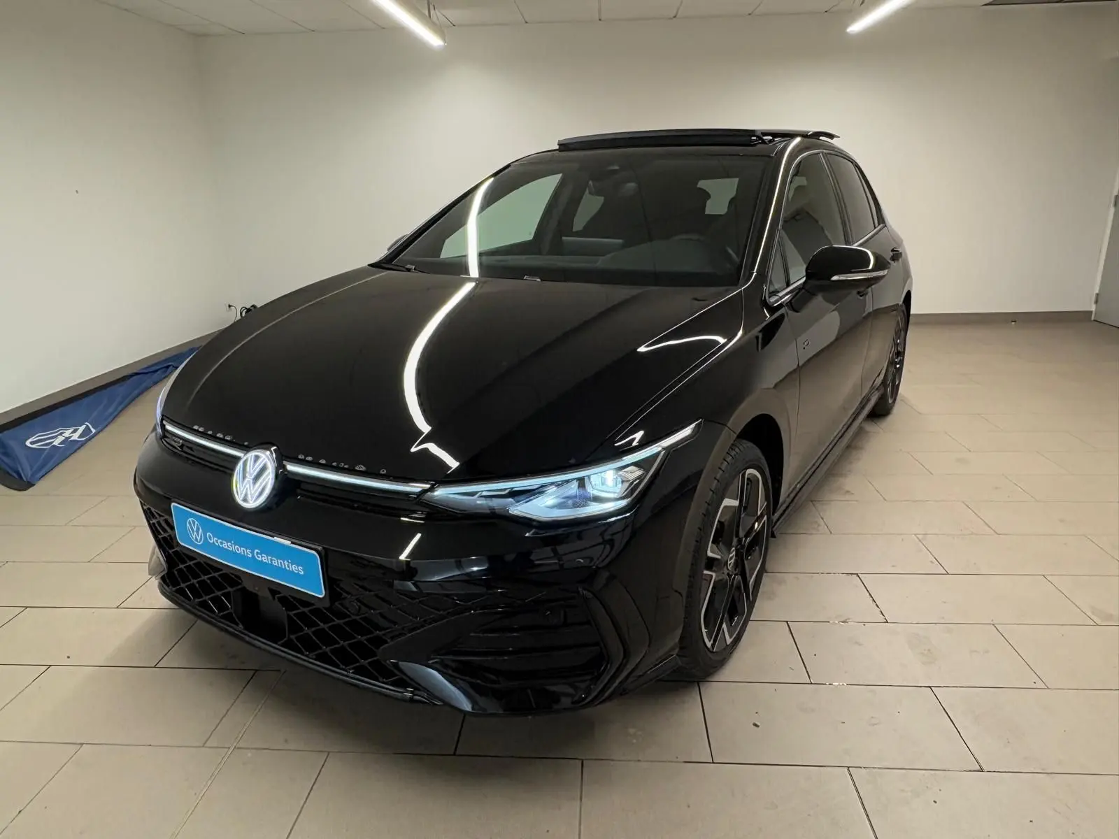 Volkswagen Golf 2.0 TDI R-Line noir grenadille vue 3/4 avant avec phares allumés dans un intérieur neutre.