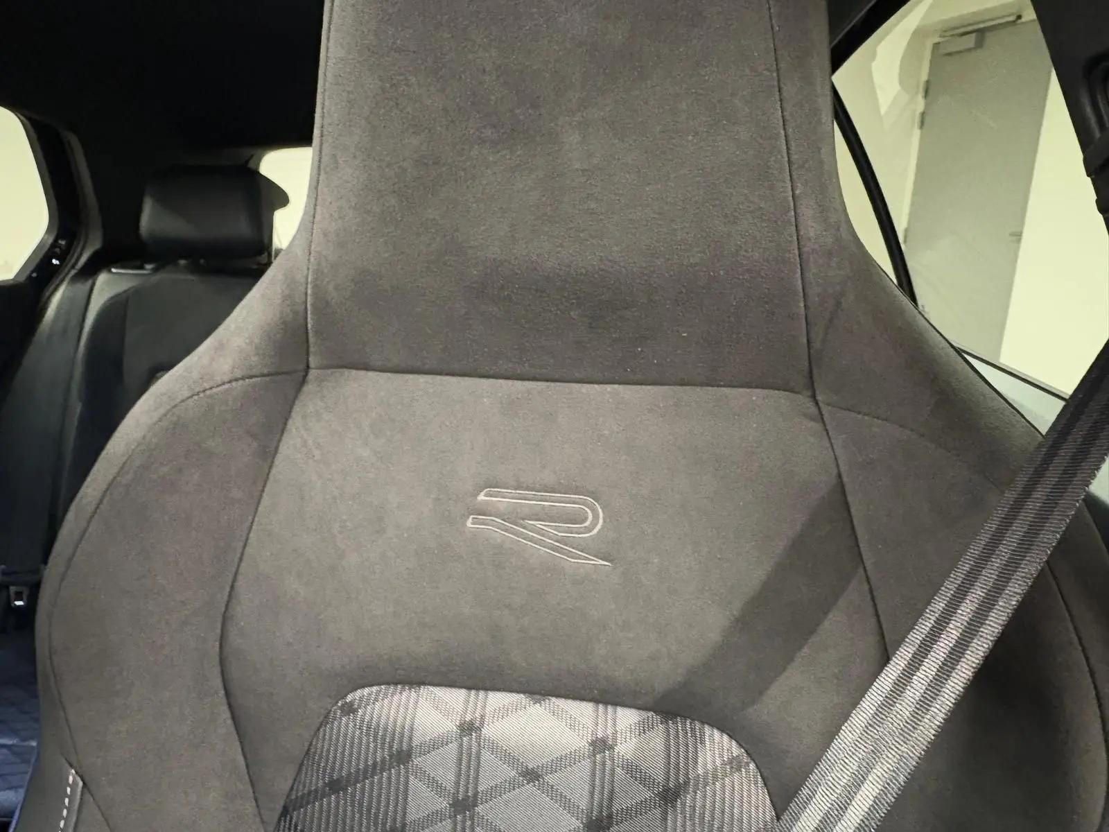 Gros plan sur le siège avant en alcantara noir avec logo R, ceinture de sécurité visible à droite.