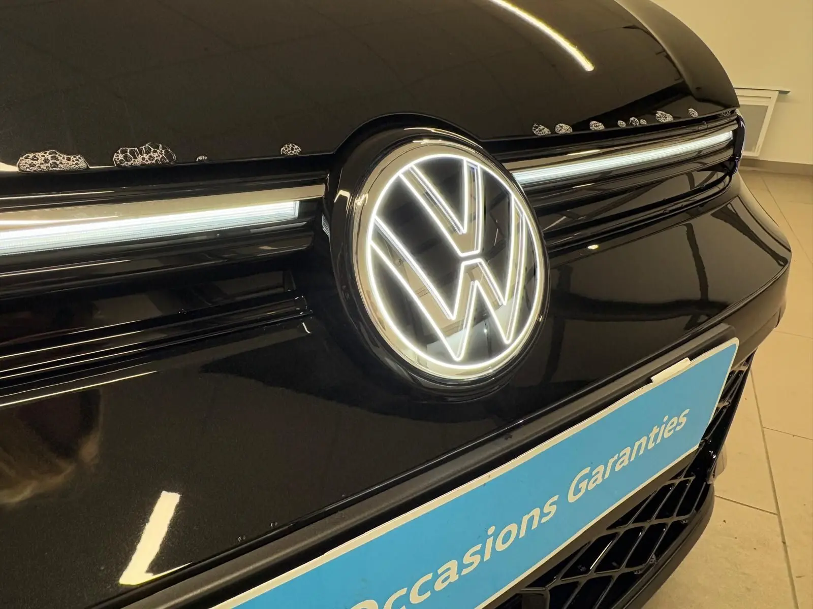 Gros plan sur la calandre avant noire grenadille d’une Volkswagen Golf 2.0 TDI avec logo VW lumineux.