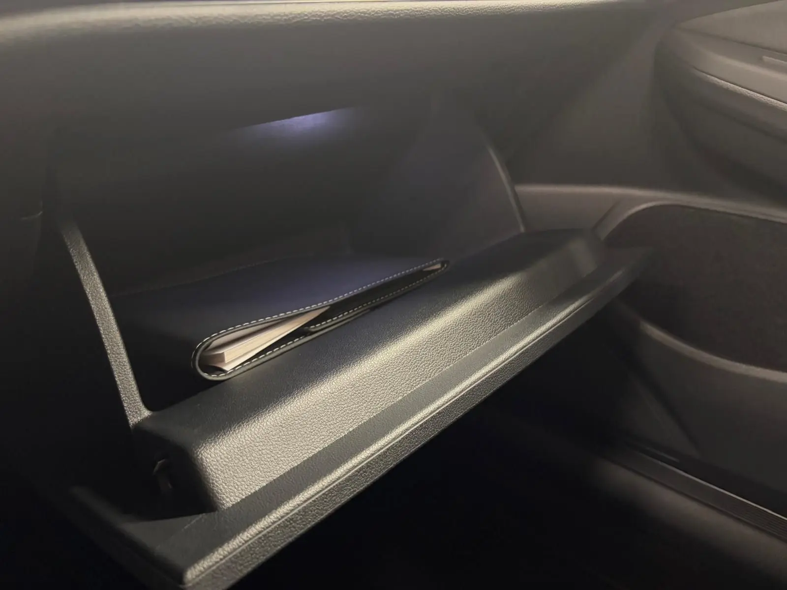 Gros plan sur la boîte à gants ouverte de la Volkswagen Golf 2.0 TDI 150 DSG7 R-Line noir Grenadille, intérieur sombre.