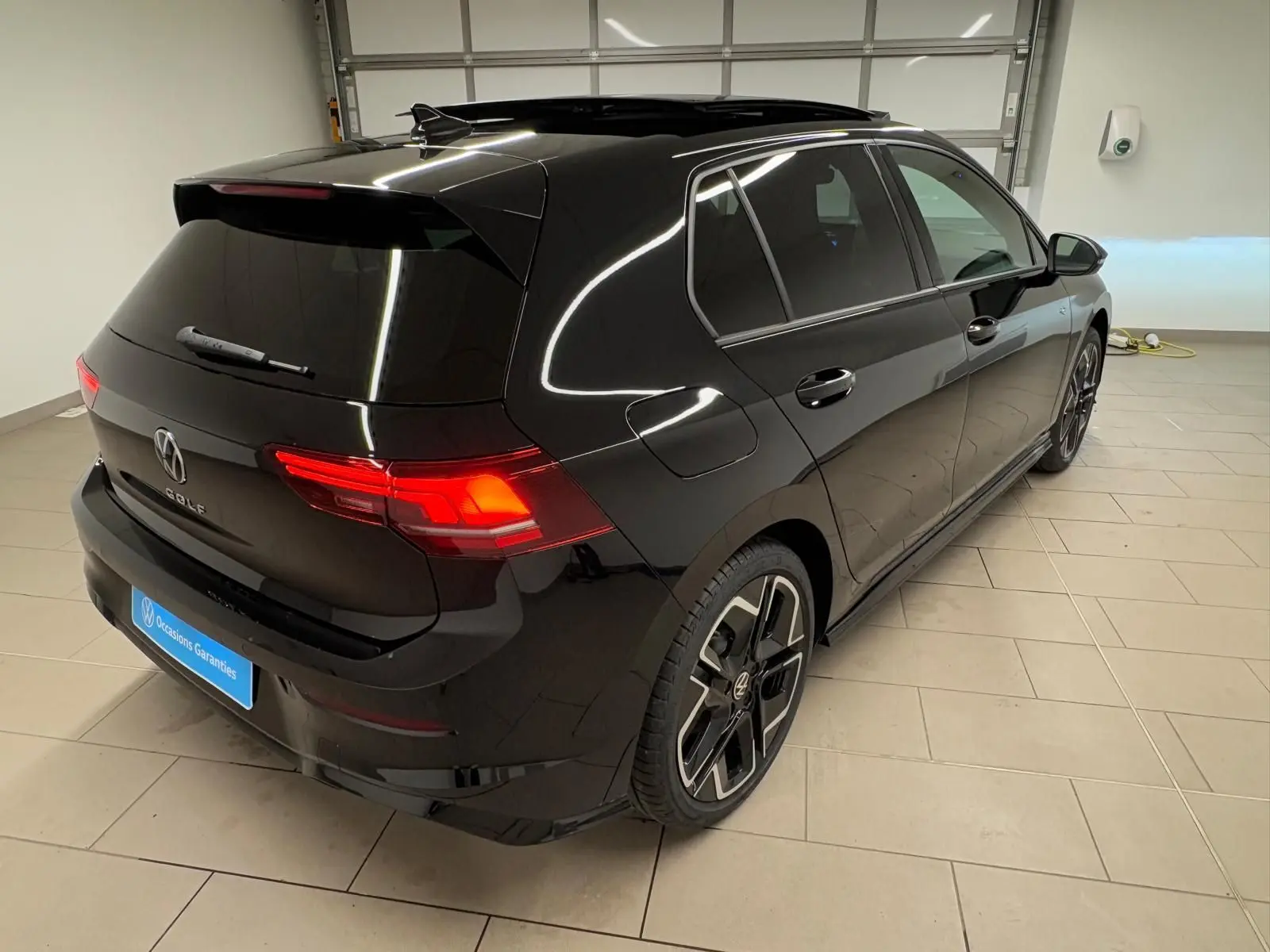Vue 3/4 arrière droite d'une Volkswagen Golf 2.0 TDI R-Line noire Grenadille avec toit ouvrant panoramique en intérieur showroom.