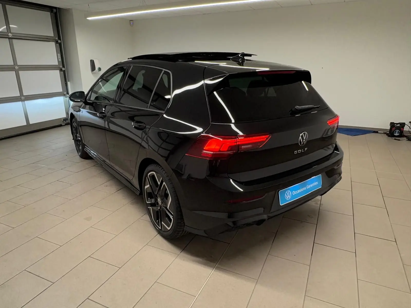 Vue 3/4 arrière droite d'une Volkswagen Golf 2.0 TDI R-Line noir grenadille avec feux arrière allumés en intérieur.