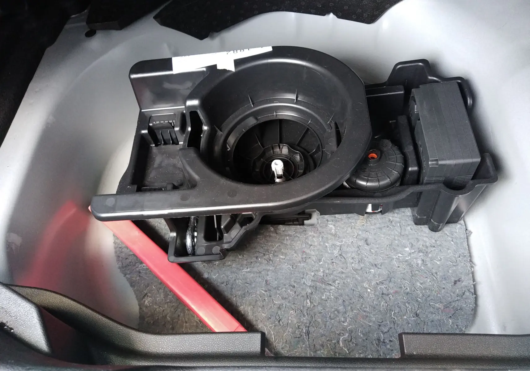 Gros plan sur le rangement sous le plancher du coffre d’un Jeep Avenger gris, montrant un support d’outils noir.