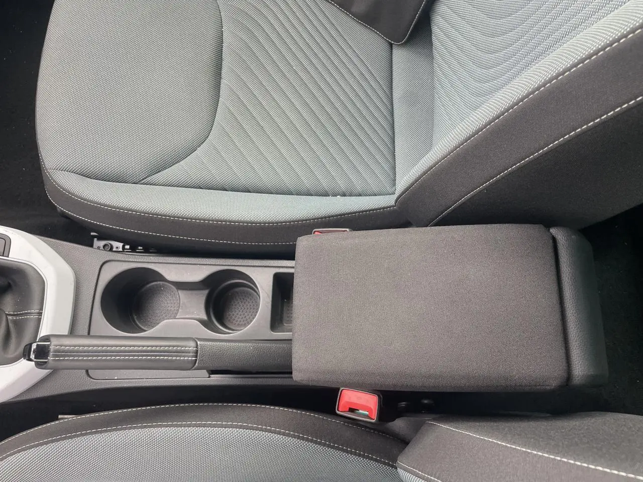 Vue plongeante sur l'accoudoir central et les sièges gris foncé avec coutures blanches d'une SEAT IBIZA blanche 2025.