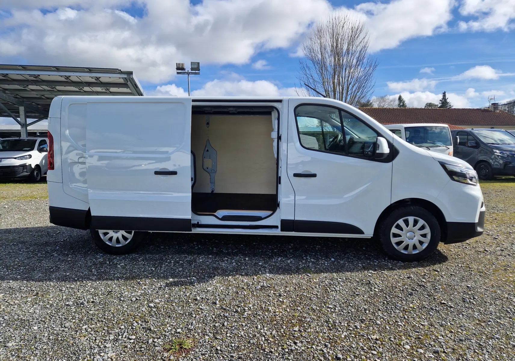 Vue latérale droite d’un utilitaire blanc Nissan Primastar 2025 avec porte coulissante ouverte montrant l’intérieur vide.