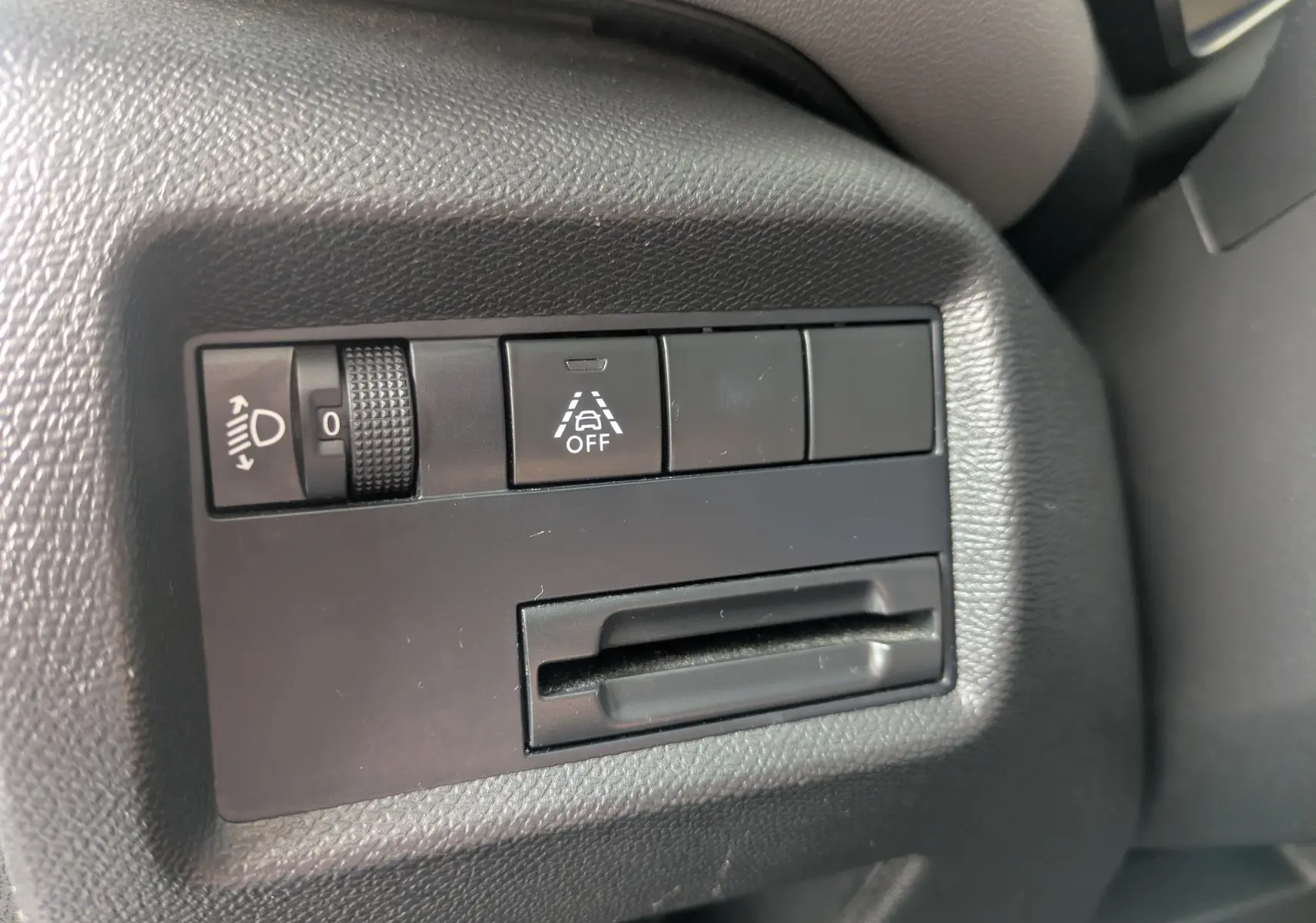 Gros plan sur les commandes noires du tableau de bord côté conducteur du Citroën C5 Aircross blanc, avec réglage des phares et bouton d'assistance.