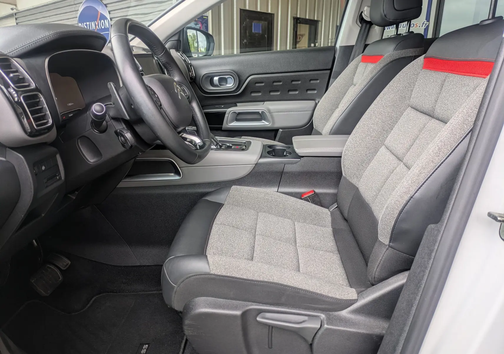 Vue intérieure côté conducteur du Citroën C5 Aircross blanc 2020, sièges tissu gris avec bande rouge et volant cuir noir.