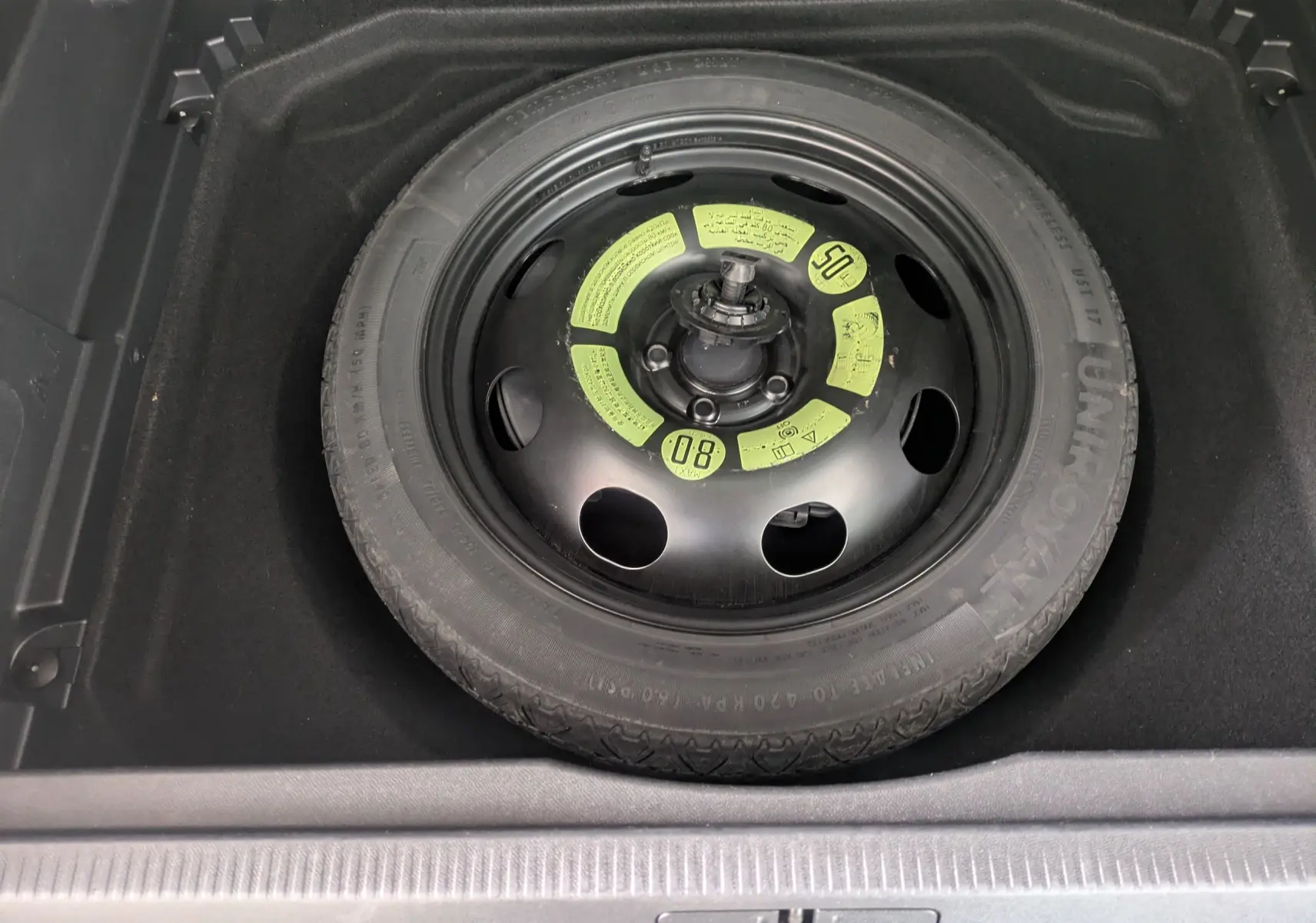 Roue de secours noire avec marquages jaunes, logée dans le coffre d'un Citroën C5 Aircross blanc.