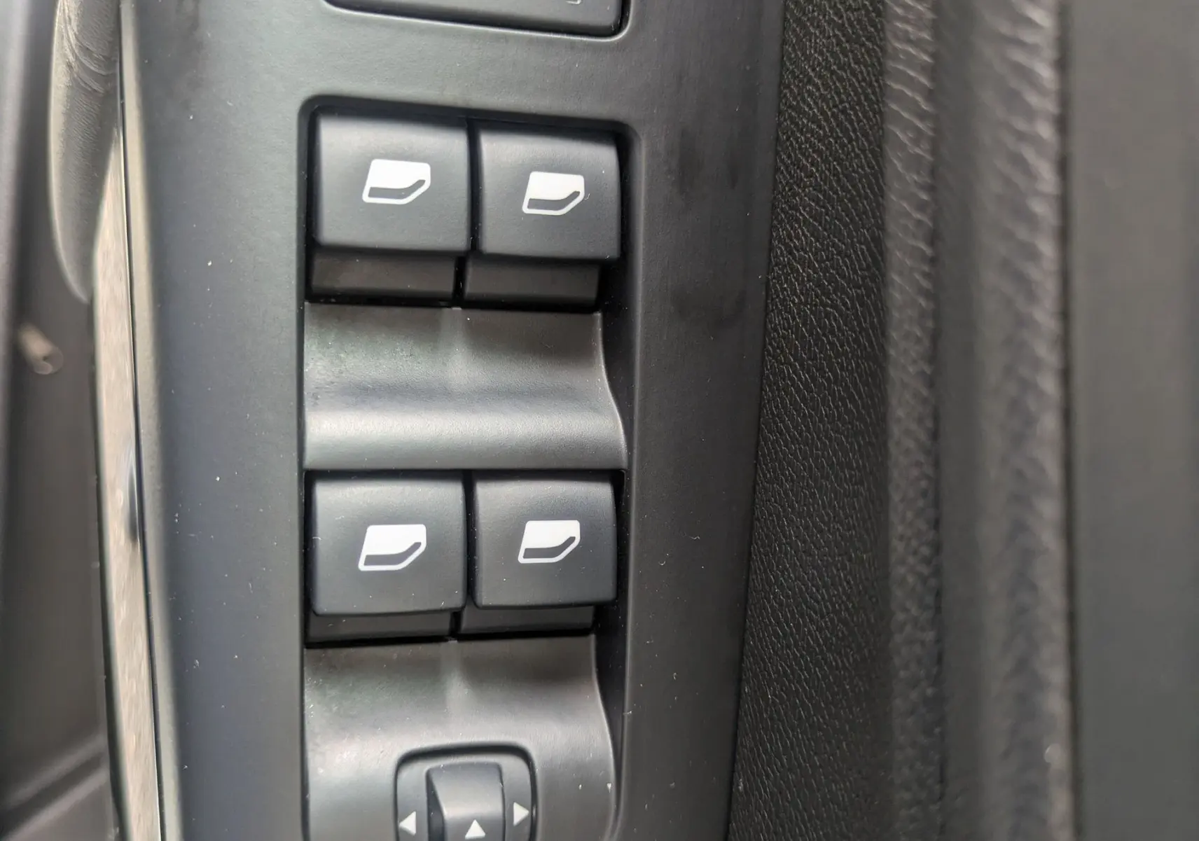 Vue rapprochée des commandes de lève-vitres et réglages des rétroviseurs sur la porte côté conducteur d'un Citroën C5 Aircross blanc.