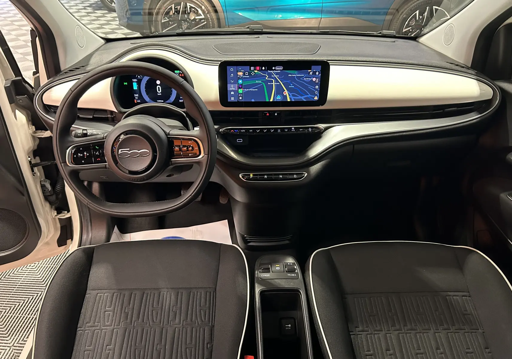 Intérieur de la Fiat 500 électrique blanche 2023, vue frontale du tableau de bord et sièges noirs avec logo FIAT.