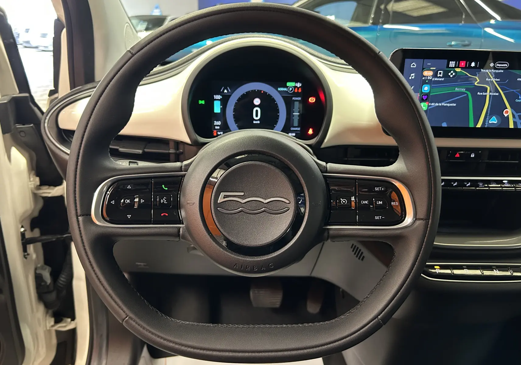 Vue centrée sur le volant noir de la Fiat 500 électrique blanche, avec tableau de bord numérique et écran tactile visible.