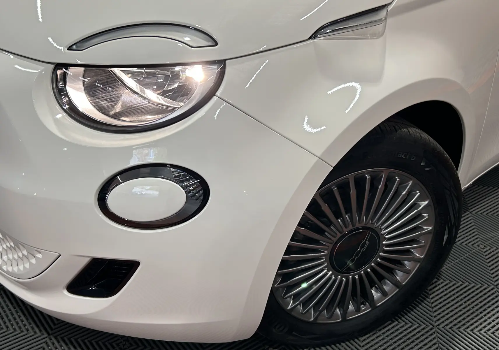 Gros plan sur l’avant droit blanc du FIAT 500 électrique 2023, mettant en valeur le phare et la jante stylisée.