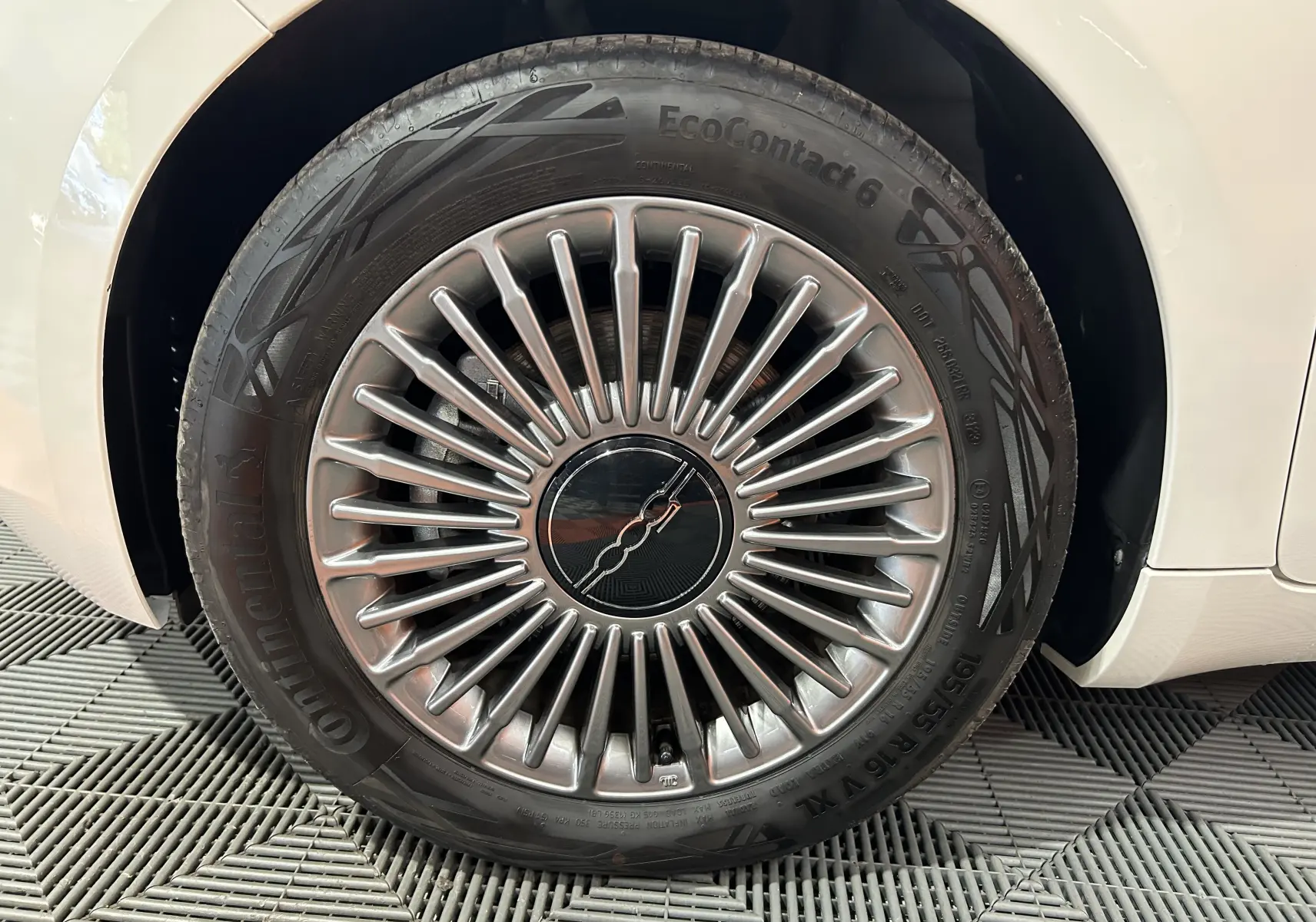 Gros plan sur la roue avant droite d'une FIAT 500 électrique blanche, mettant en valeur la jante argentée au design rayonné.