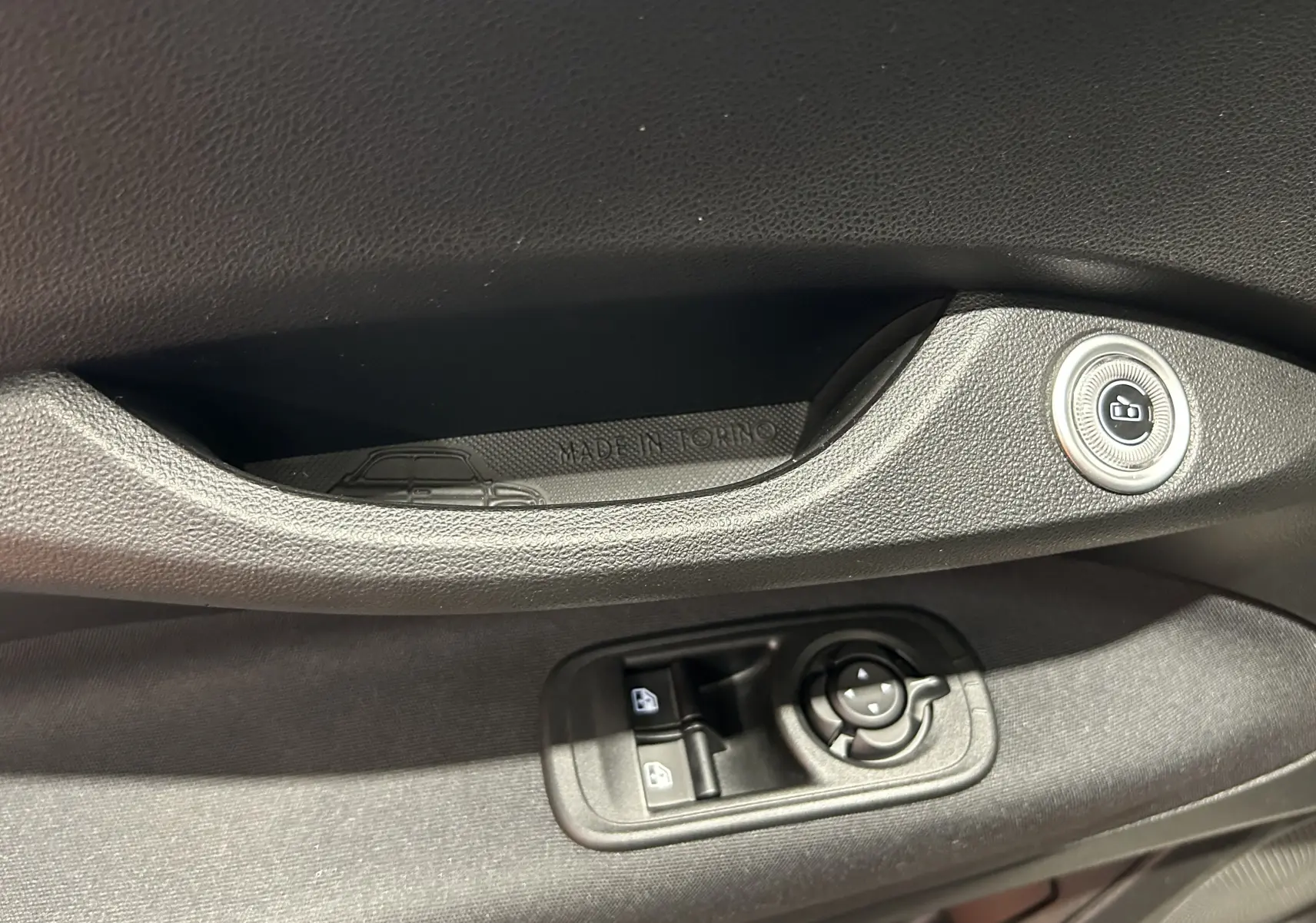 Détail de la porte côté conducteur de la Fiat 500 électrique blanche 2023 avec commandes de vitres et inscription "Made in Torino".