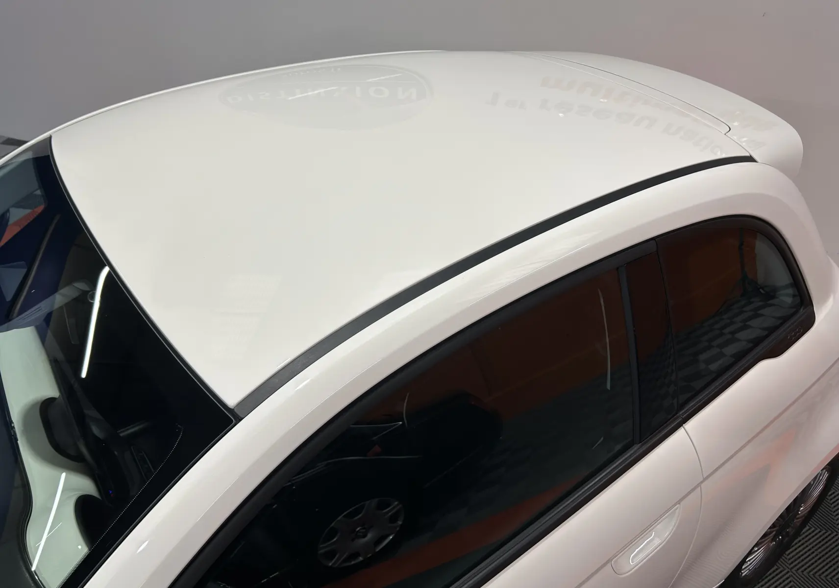 Vue plongeante côté gauche sur la FIAT 500 électrique blanche 2023, mettant en valeur son toit lisse et ses vitres teintées.
