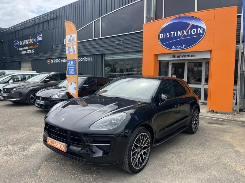 Vue 3/4 avant droite d'un Porsche Macan noir brillant avec jantes sport devant un concessionnaire Distinxion.
