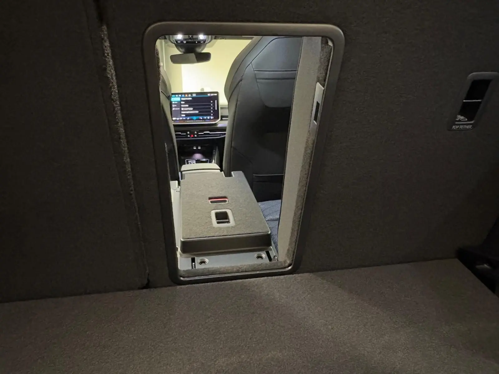 Vue intérieure depuis le coffre vers l'avant, montrant l'ouverture centrale et l'écran du tableau de bord d'une Volkswagen Golf noir grenadille.
