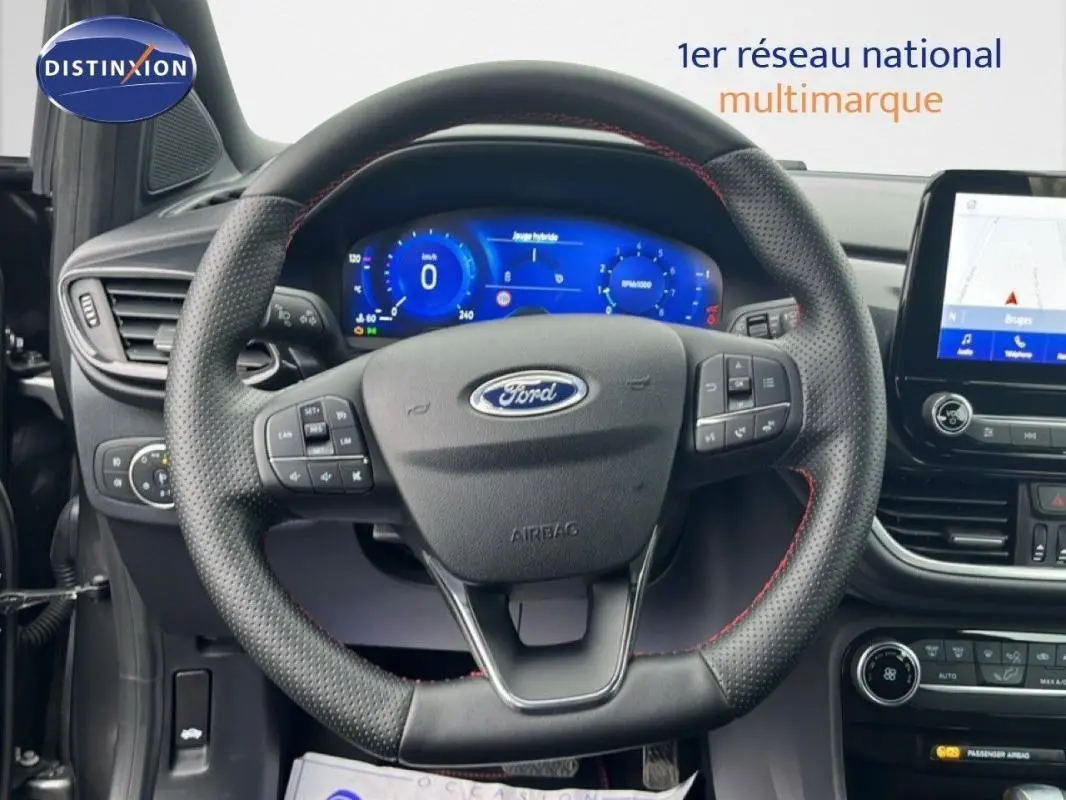 Vue intérieure centrée sur le volant perforé de la Ford Puma 2024 avec tableau de bord numérique et écran tactile GPS.