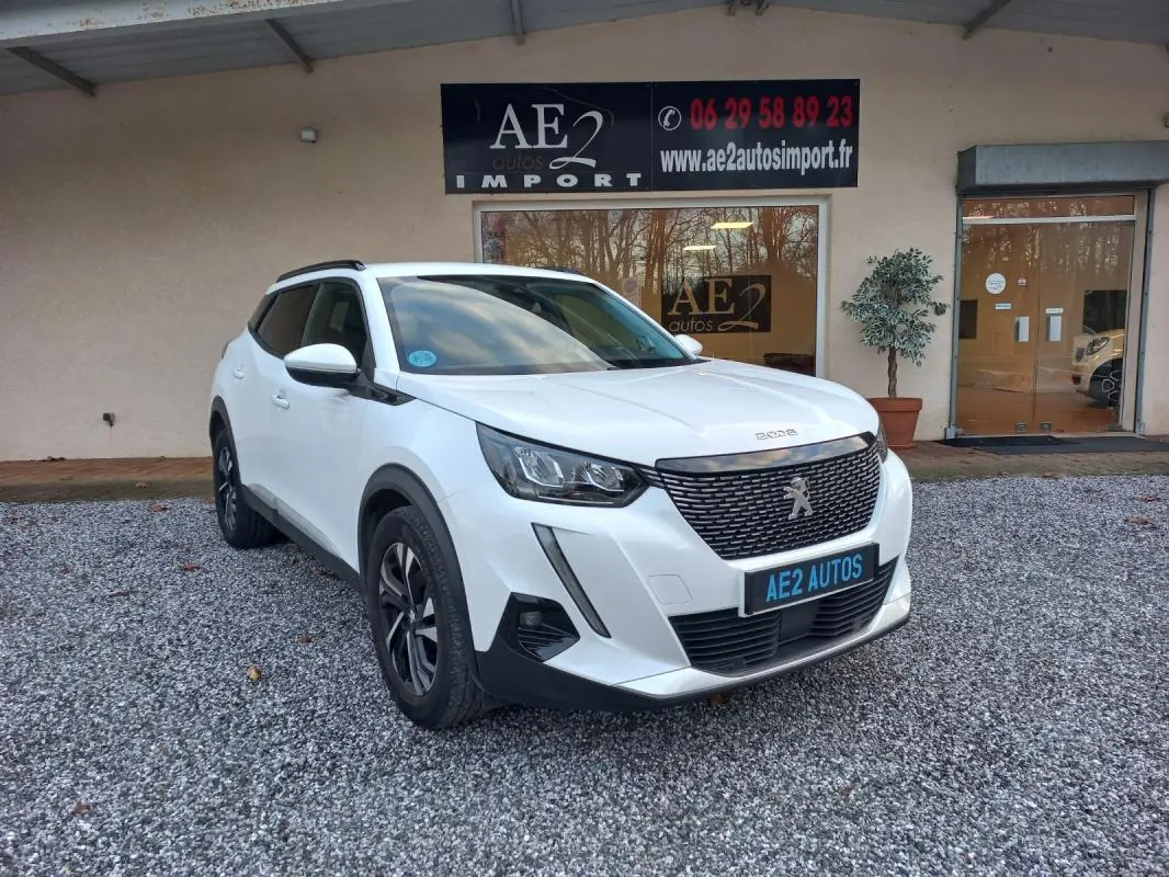 Peugeot 2008 blanc vue 3/4 avant droit, avec calandre noire et jantes alliage, stationné devant un bâtiment.