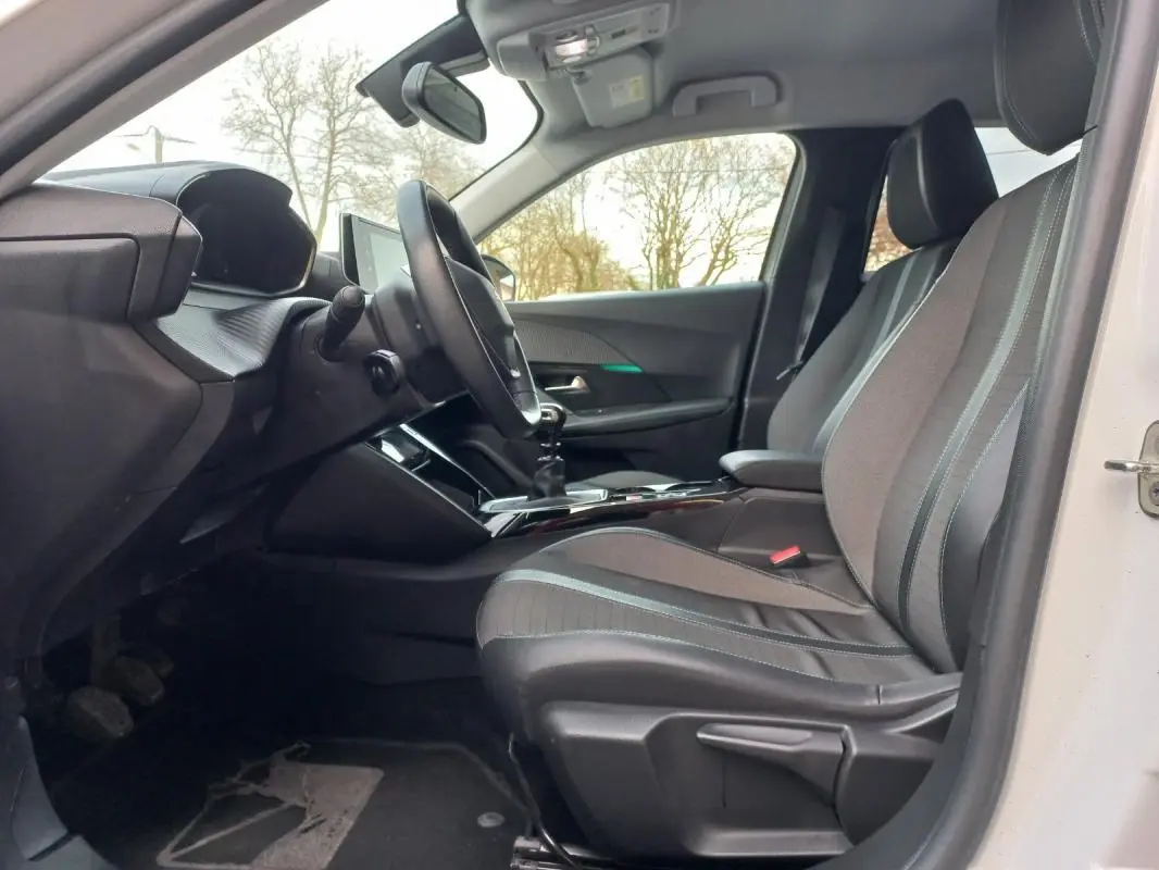 Vue intérieure côté conducteur de la Peugeot 2008 blanche 2021, montrant les sièges et le tableau de bord moderne.