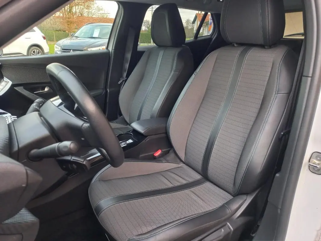 Vue intérieure côté conducteur du Peugeot 2008 blanc 2021, sièges tissu gris avec inserts noirs et volant visible.