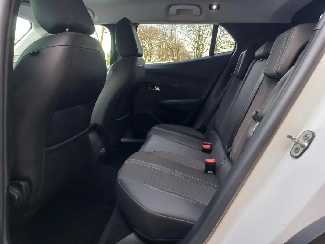 Vue intérieure côté arrière droit du Peugeot 2008 blanc, montrant les sièges arrière en tissu et cuir noir.