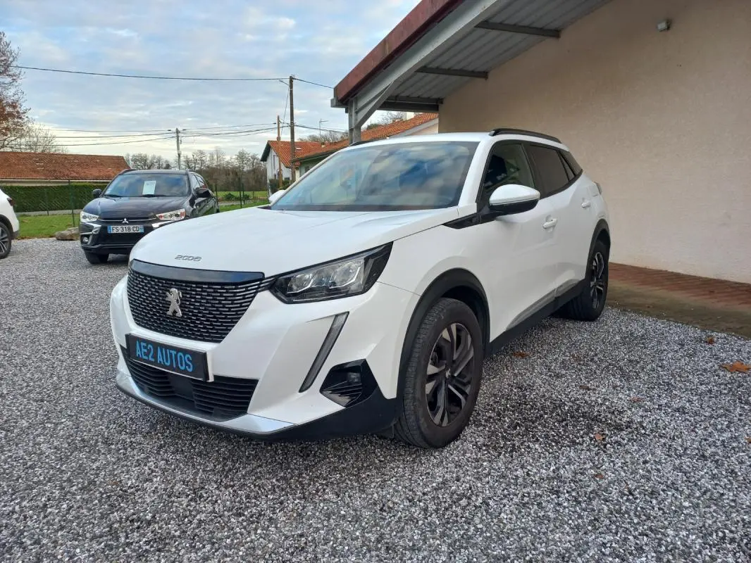 Peugeot 2008 blanc en 3/4 avant droit, avec calandre noire et jantes alliage foncé, stationné sur gravier.